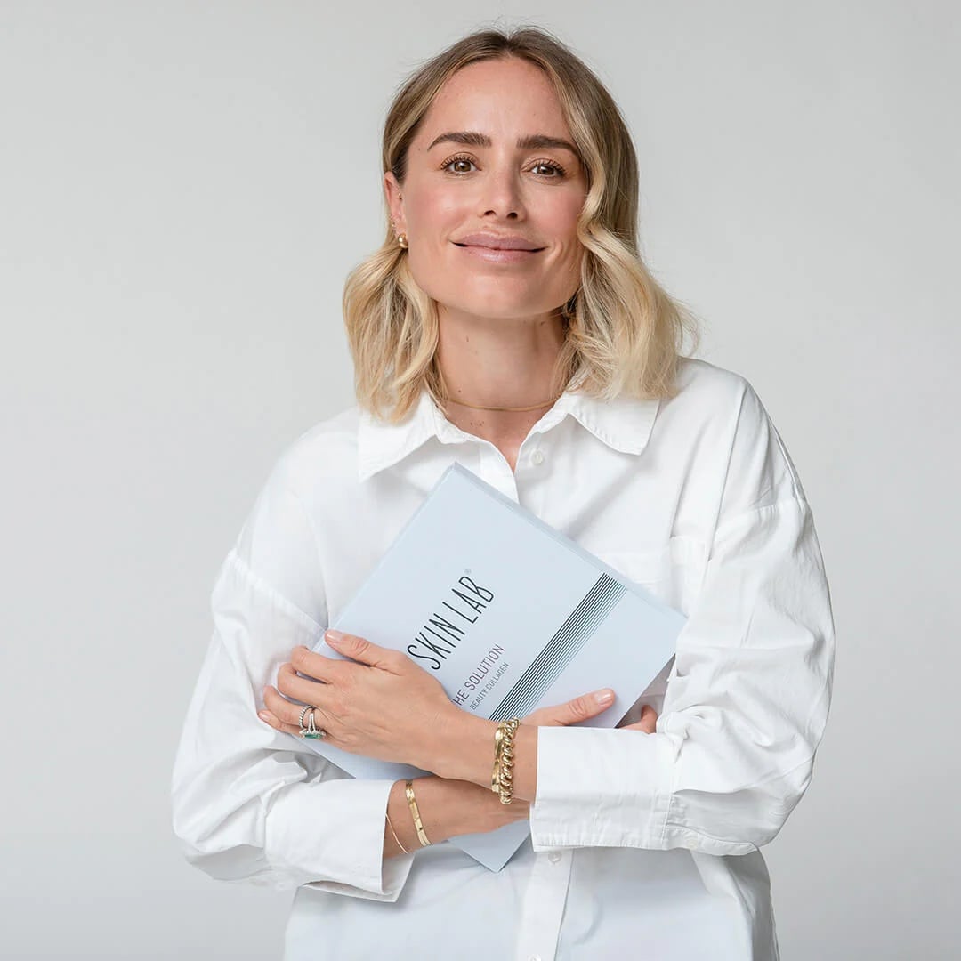 Anine Bing hält The Solution Beauty Collagen und lächelt